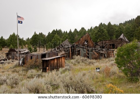 Tattered US Flag on an old wooden flag pole along with a Montana flag fly over this neglected Montana ghost town