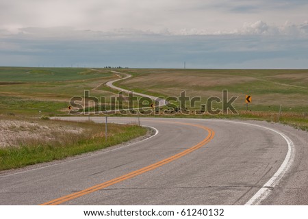 Winding, curvy road through rural America runs through pasture land.  Cows are hanging out below the first curve.