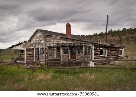 Abandoned ranch house built of logs and wood surrounded by a log fence on a rainy day
