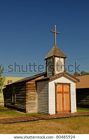 Rustic church with wooden cross on the steeple and another cross on the wooden doors.  Church is made of logs and wood and is on display in an outdoor museum in Montana.