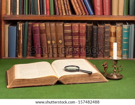 Antique leather books, tin candlestick and magnifying glass on green blotter.