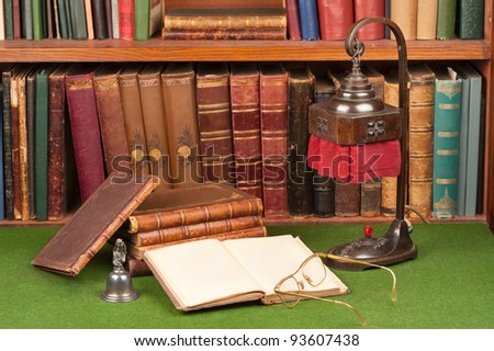 Antique leather books, lamp and reading glasses on green blotter.