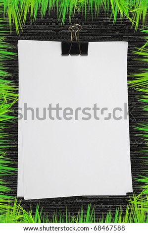 Black clip and white blank note paper with green grass