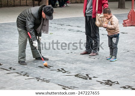 BEIJING, CHINA - MARCH 26: Kid looking on Chinese letters written by old man practising calligraphy in Temple of Heaven park area on March 26, 2013 in Beijing