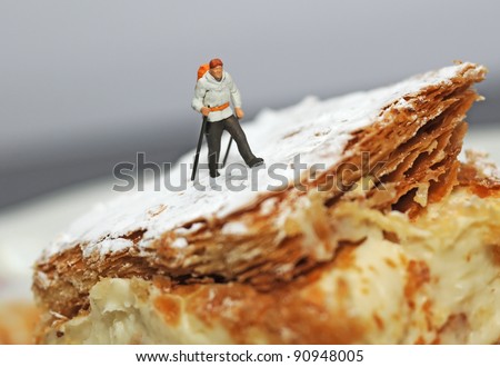 Small hiker figure walking on a piece of cake with castor sugar imitating snow