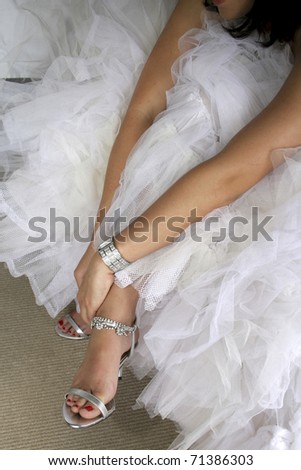 Bride in white wedding dress putting on silver shoes