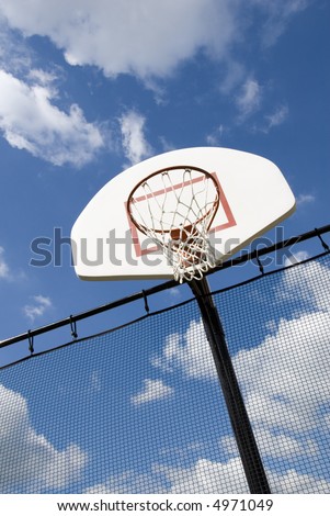 A basketball hoop in a children\'s playground stands against a partly cloudy blue sky.
