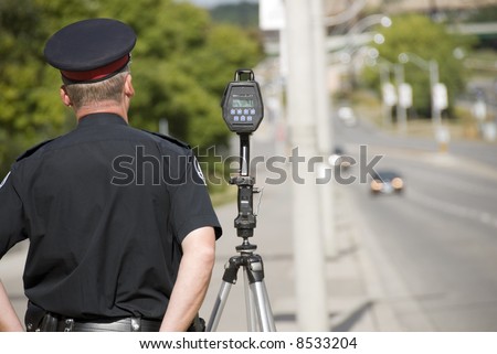 A North American policeman waits to catch speeding drivers with a radar gun. (Shot with minimum depth of field. Focus is on the police officer and radar gun.)