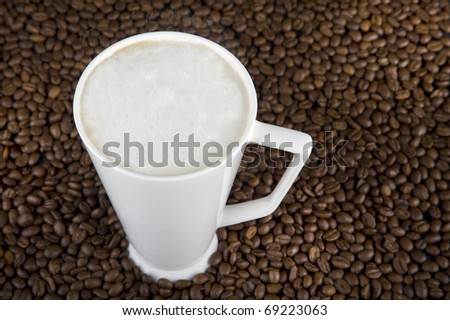mug filled with hot coffe with cream on brown beans background