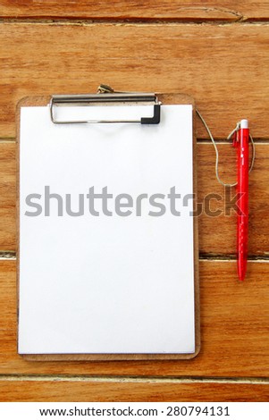 Clipboard with paper and red pen on wood board