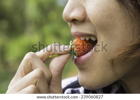Macro view of a pretty young female eating fresh strawberry