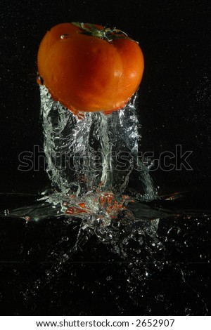 The red tomato and sparks are shined by flash at falling in water on a black background. The picture is turned