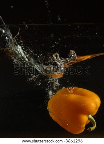 Sweet pepper and sparks are shined by flash at falling in water on a black background
