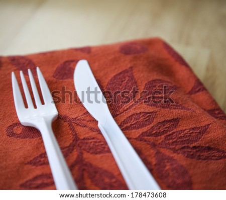 Plastic knife and fork on orange cloth napkin on kitchen table