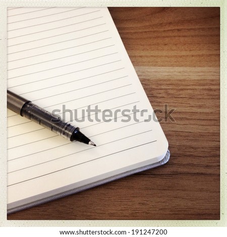 Instagram style image of a blank notebook and ink pen on a wooden desk