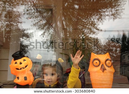 Authentic image of a toddler girl waving at a window in a Halloween costume  in the Instagram filtered style - soft focus