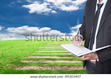 Asian businessman writing on notebook on blue sky field.