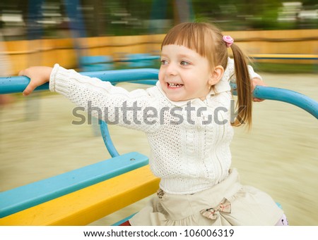 Cute cheerful little girl is riding merry-go-round, background blurred with motion
