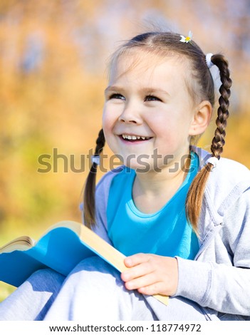 Cute little girl reads a book in autumn park