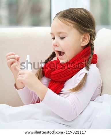 Little girl spraying her nose with nasal spray while sitting on sofa