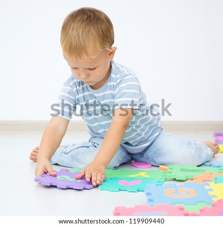 Little boy is putting together a big puzzle while sitting on the floor