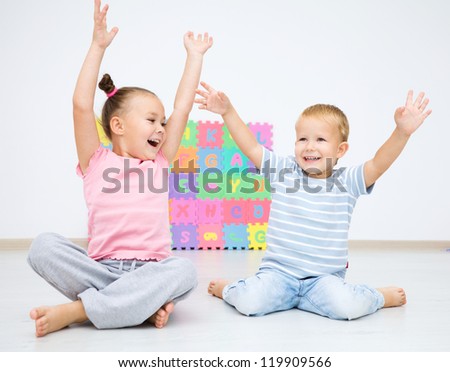 Cute children are sitting on floor in preschool rising their hands up