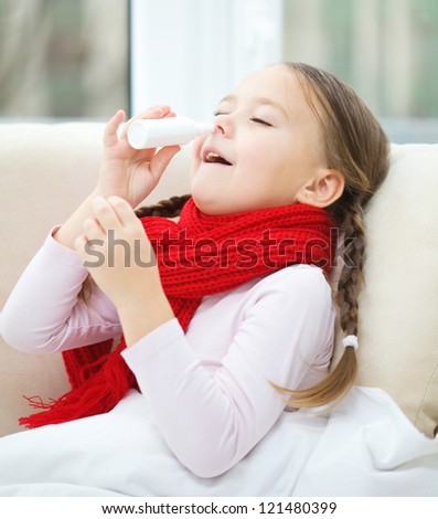 Little girl spraying her nose with nasal spray while sitting on sofa