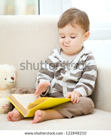 Little boy is reading book while sitting on couch, indoor shoot