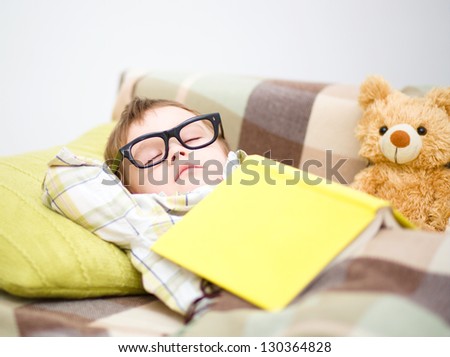 Cute little boy is sleeping in front of his teddy bears wearing glasses and put off a big book