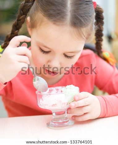 Cute little girl is eating ice-cream in parlor