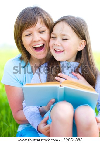 Mother is reading book with her daughter, outdoor shoot