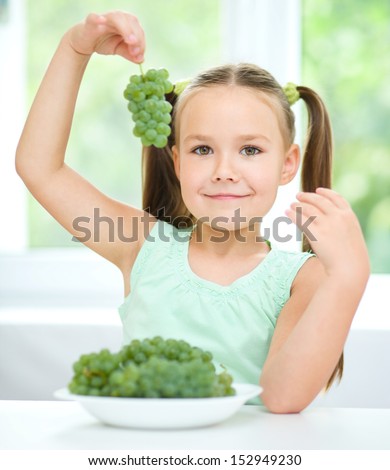 Cute little girl is eating green grapes, isolated over white