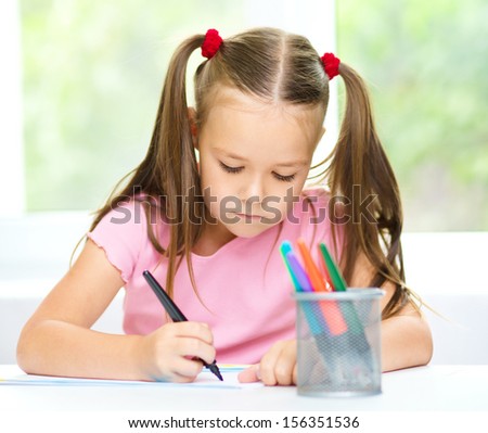 Cute cheerful child drawing using felt-tip pen while sitting at table