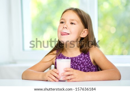 Cute little girl is licking her lips while drinking milk