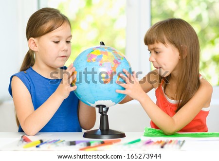 Little girls are examining globe while sitting at table