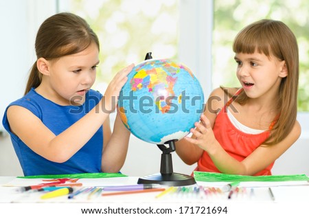 Little girls are examining globe while sitting at table