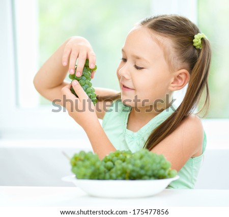 Cute little girl is eating green grapes, isolated over white