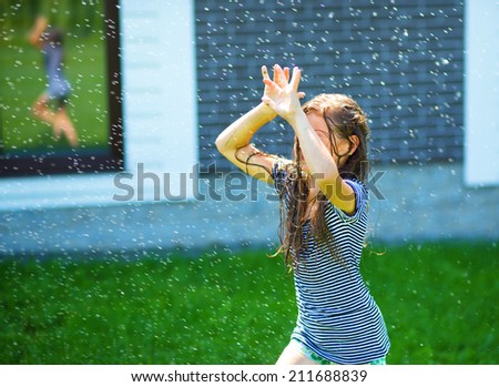 Happy girl is playing under rain on backyard