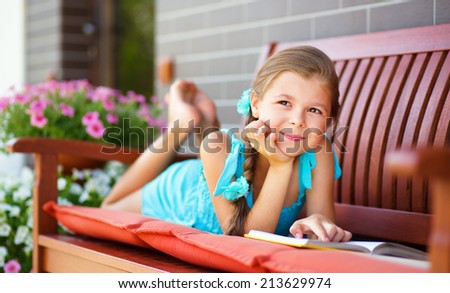 Cute little girl is reading a book while laying on bench