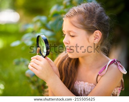 Young girl is looking at flower through magnifier, outdoor shoot