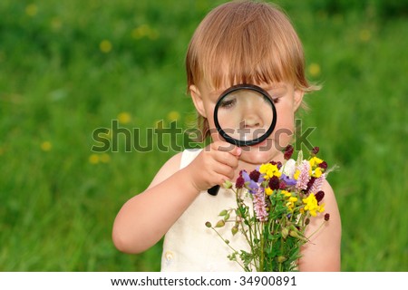Cute little girl looking at bouquet of field flowers through magnifying glass