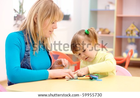 Teacher and cute little girl play with plasticine in preschool