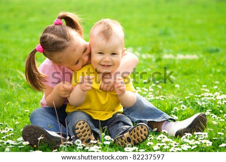 Two children are sitting on green meadow and smile