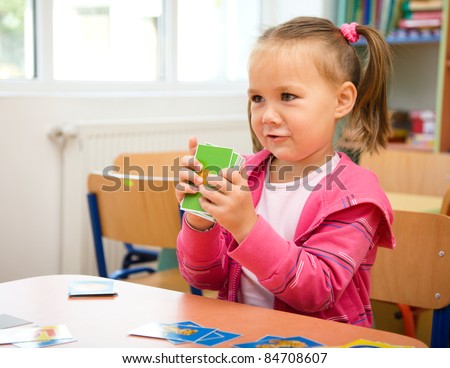 Cute little girl is playing with educational cards while sitting at table