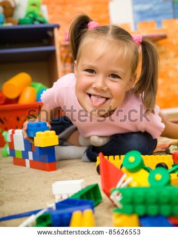 Little girl is showing tongue while playing with building bricks in preschool