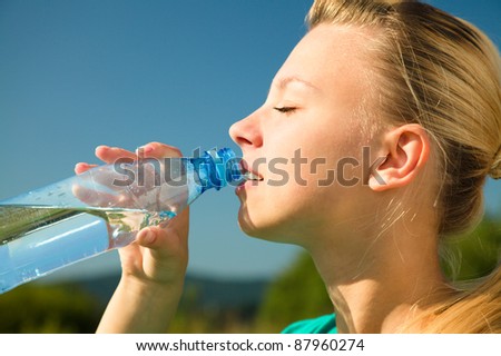 Young woman is drinking water from plastic bottle outdoors