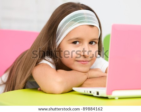 Cute little girl is sitting at table with her pink laptop