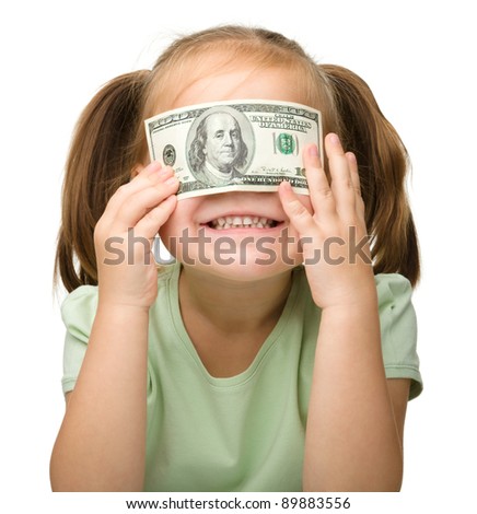 Cute little girl is covering her eyes with dollars, isolated over white
