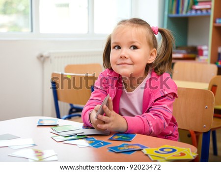Cute little girl is playing with educational cards while sitting at table