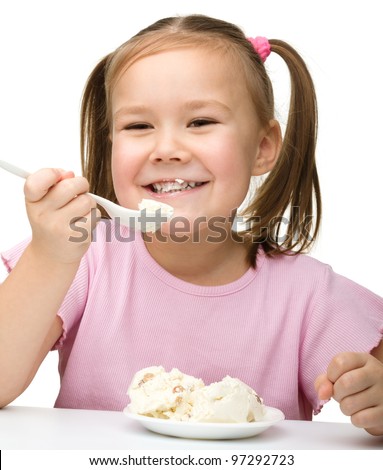 Cute little girl is eating cottage cheese using spoon, isolated over white